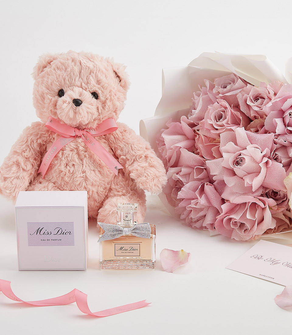 Pink roses, Miss Dior perfume, and plush teddy bear Valentine's gift set on white surface