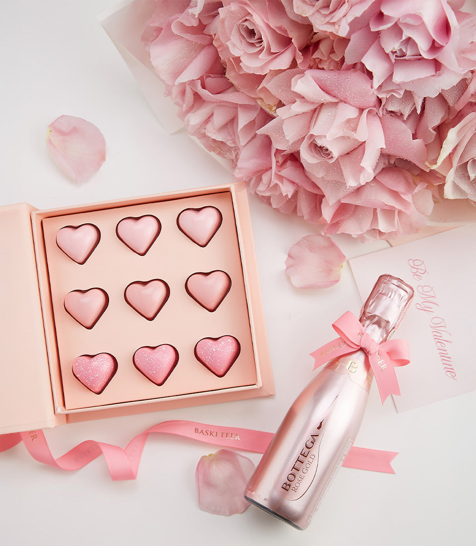 Pink champagne gift set with rose gold bottle, heart-shaped chocolates, and fresh pink roses for Valentine's Day