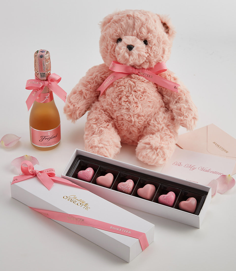 Romantic Valentine gift set with pink teddy bear, rosé champagne, and heart-shaped chocolates on white background