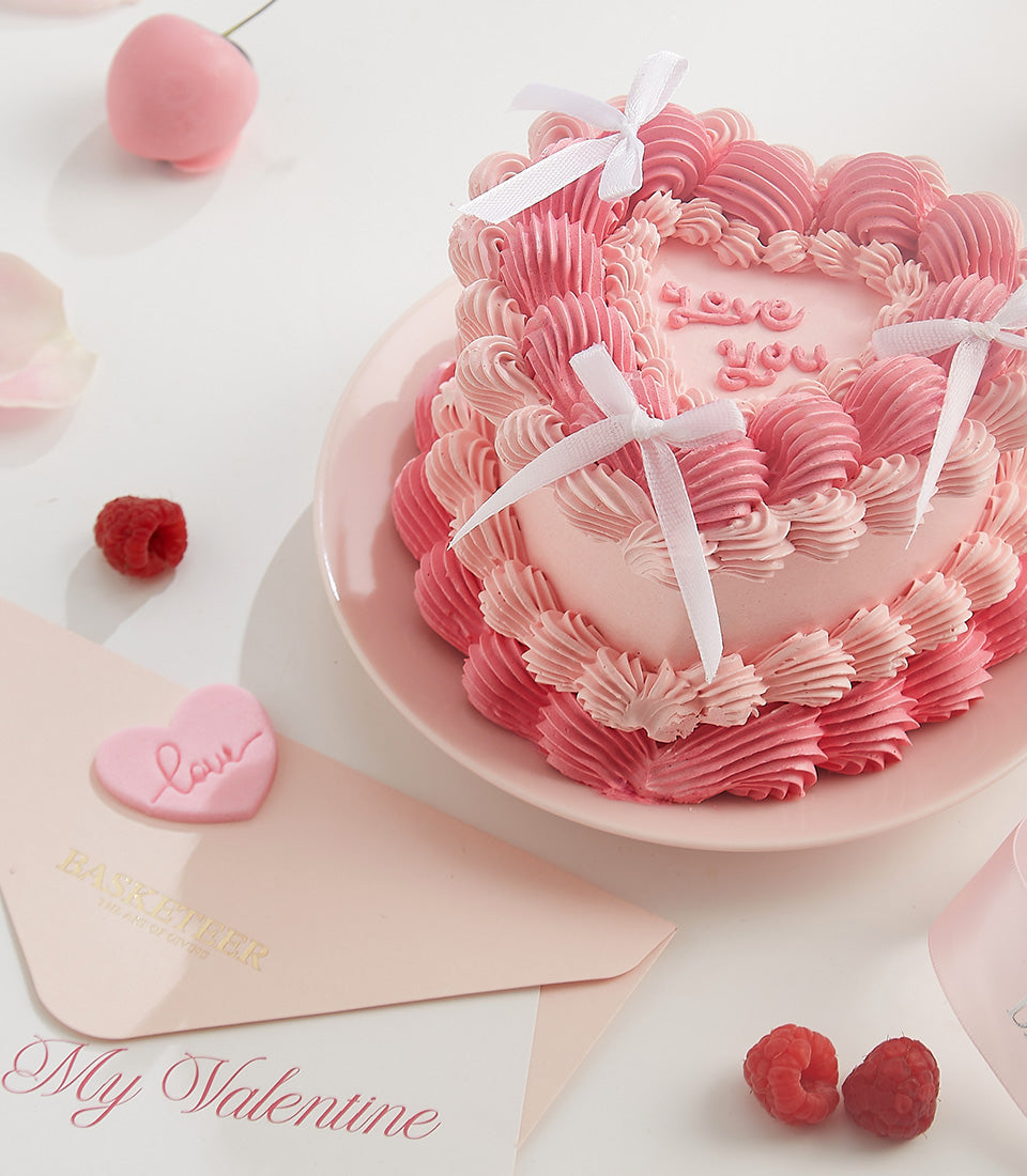 Pink heart-shaped layer cake with "love you" frosting message and white ribbon bows, served with Valentine's Day stationery