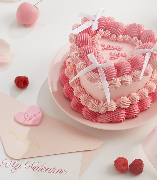 Pink heart-shaped layer cake with "love you" frosting message and white ribbon bows, served with Valentine's Day stationery