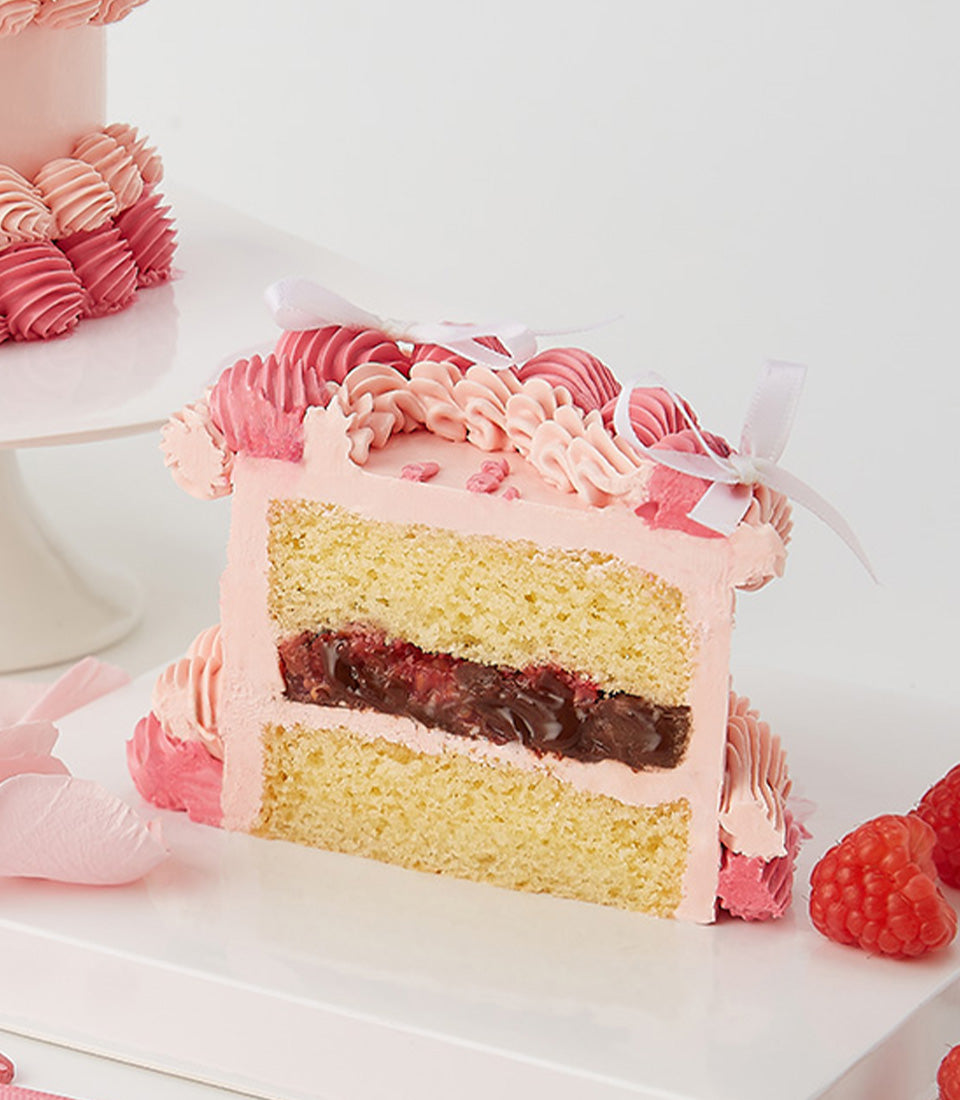 Pink raspberry layer cake slice with piped frosting swirls, Valentine's gift set with fresh roses and berries