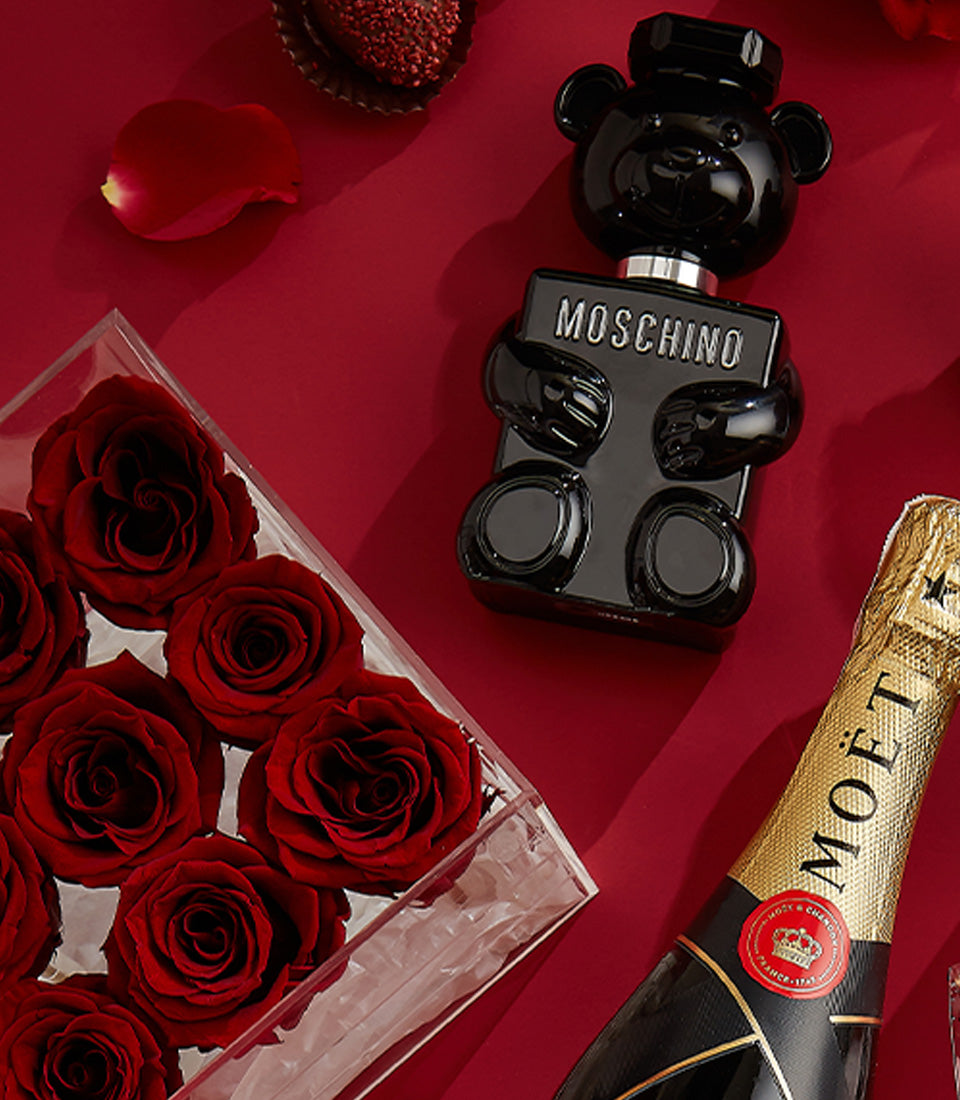 Luxury Valentine's gift set with Moët champagne, deep red roses, Moschino perfume, and chocolate truffle on rich crimson