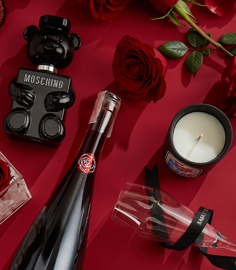 Luxury red roses with red wine, Moschino perfume, and champagne flute on deep red background for Valentine's Day