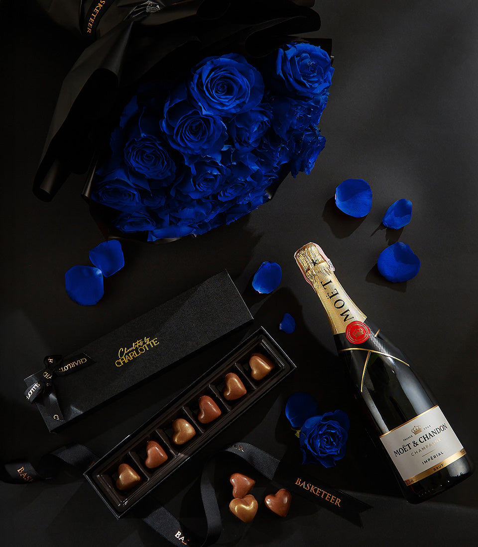 Luxury champagne, blue roses, and heart-shaped chocolates Valentine gift set on dark surface