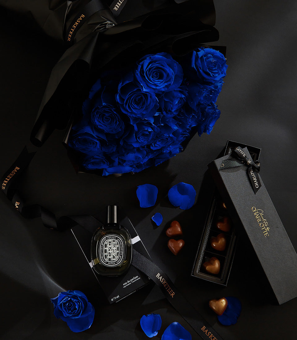 Luxury Valentine's gift set with blue roses, heart chocolates, and perfume on dark background