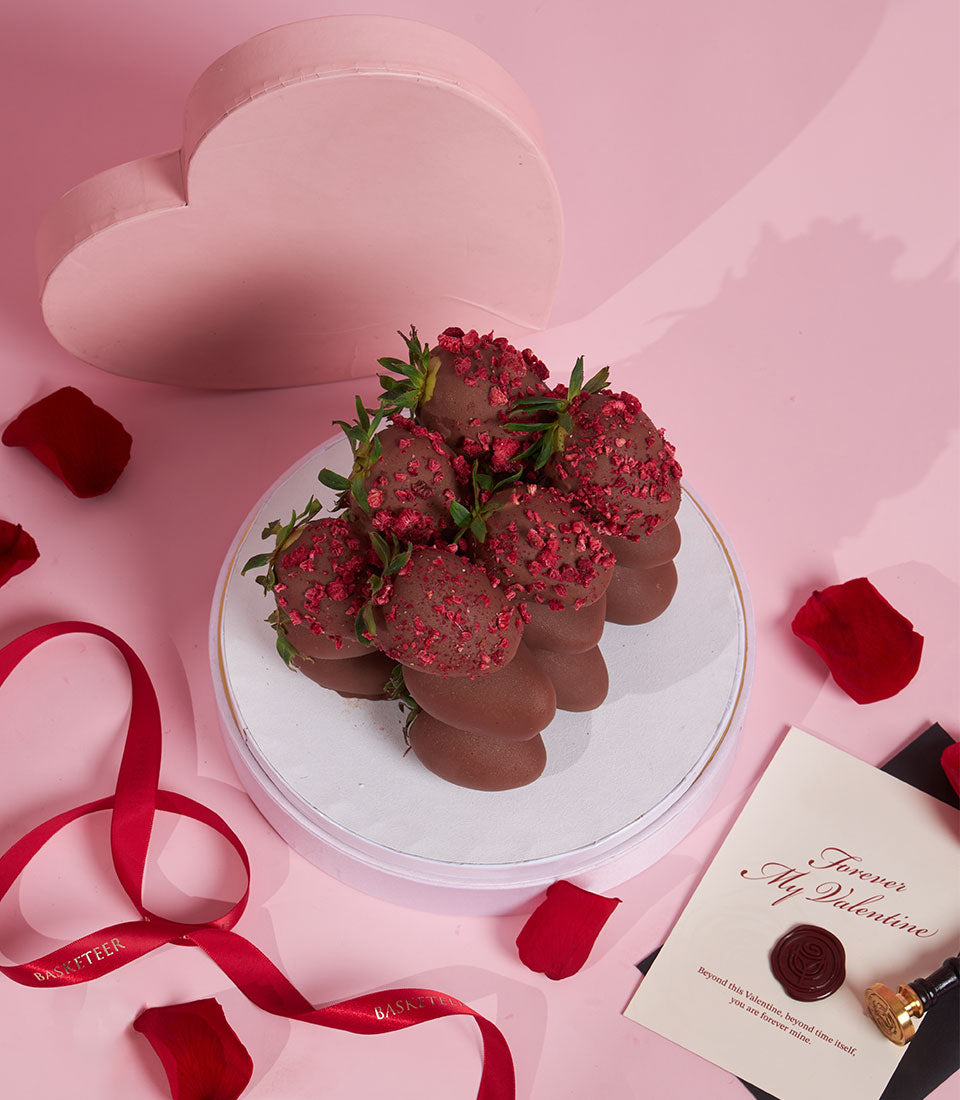 Dark chocolate-covered strawberries with raspberry pieces on gold-rimmed stand, Valentine's Day gift arrangement with rose
