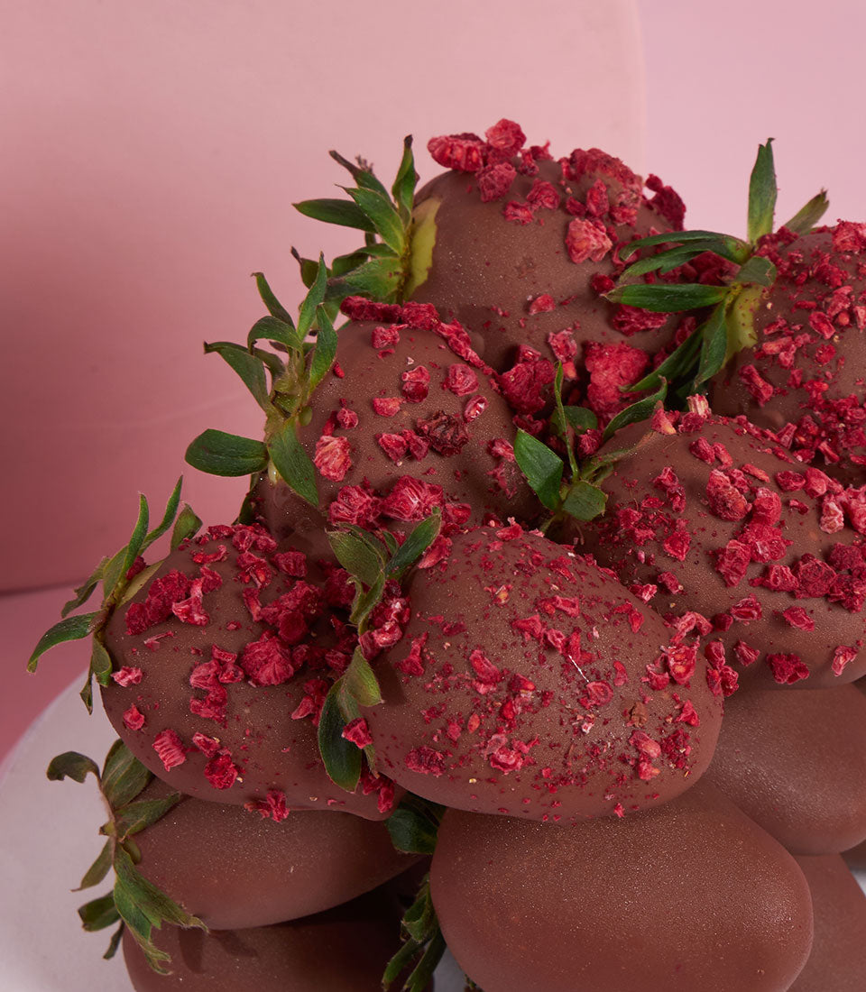 Dark chocolate-covered strawberries with raspberry pieces and fresh stems on white plate, Valentine luxury gift
