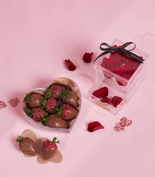 Romantic Valentine gift set with chocolate-covered strawberries in heart box and preserved red roses with petals in acrylic