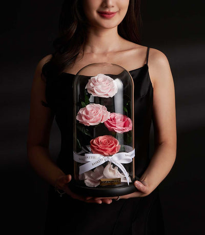 Woman holding Flowers by Basketeer eternal rose arrangement: pink roses displayed in a glass dome with ribbon. Premium flowers Bangkok, ideal rose bouquet Thailand.