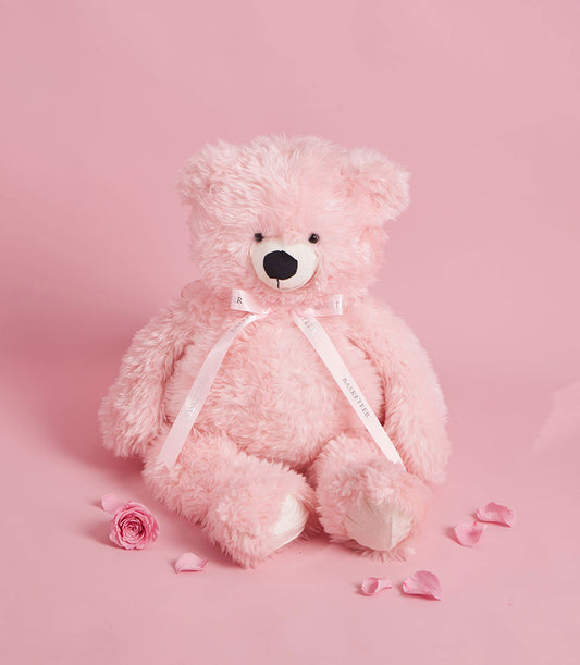 Large plush pink teddy bear with ribbon on romantic Valentine's Day gift background with rose petals