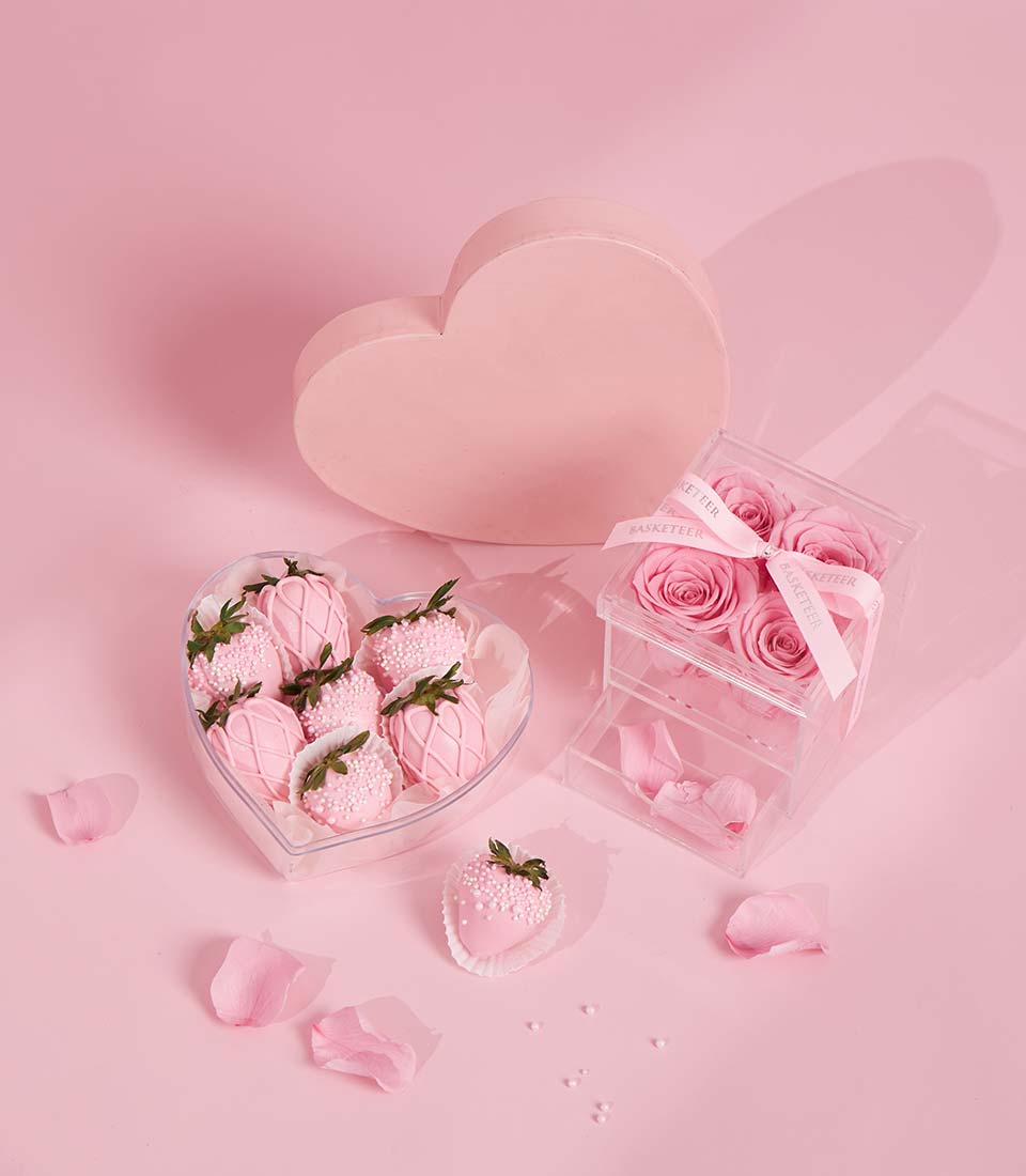 Pink chocolate strawberries, preserved roses, and rose petals Valentine gift set on pink background
