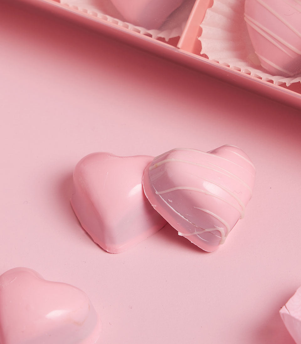 Heart-shaped artisan chocolate bonbons from Charlotte Bakery in Bangkok. Pink sweets with white drizzle, perfect for a birthday cake delivery in Bangkok or a custom cake order.