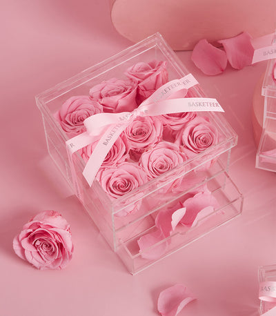 Luxury acrylic box with nine preserved pink roses, ribbon-tied with loose petals, romantic Valentine's gift