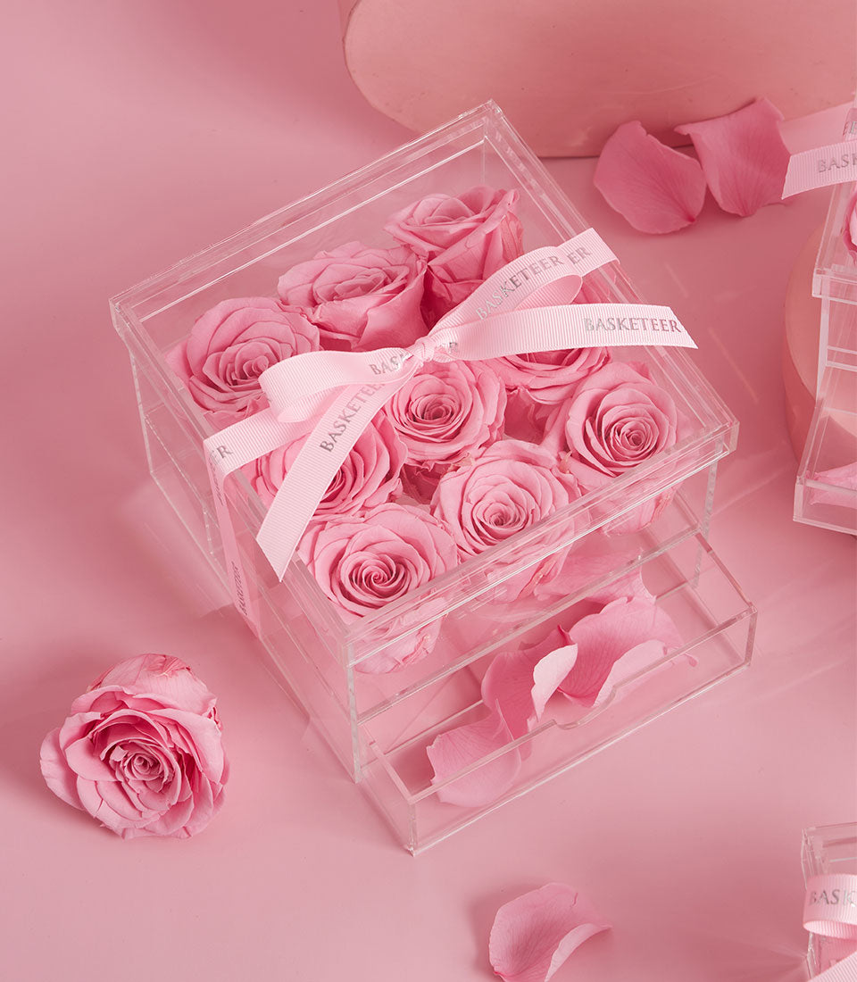Luxury acrylic box with nine preserved pink roses, ribbon-tied with loose petals, romantic Valentine's gift