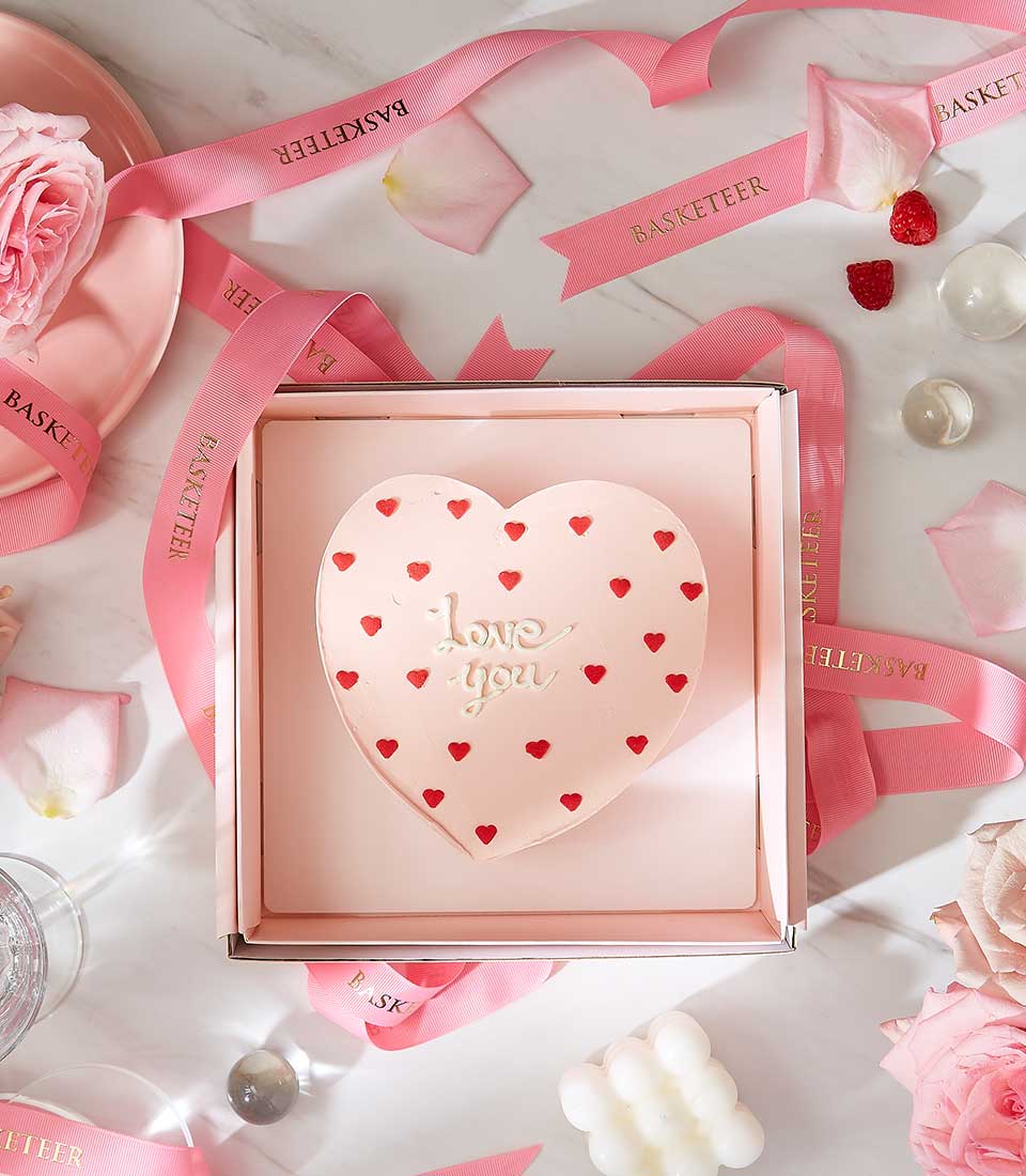Heart-shaped pink cake with red hearts and "love you" message in romantic Valentine's gift box