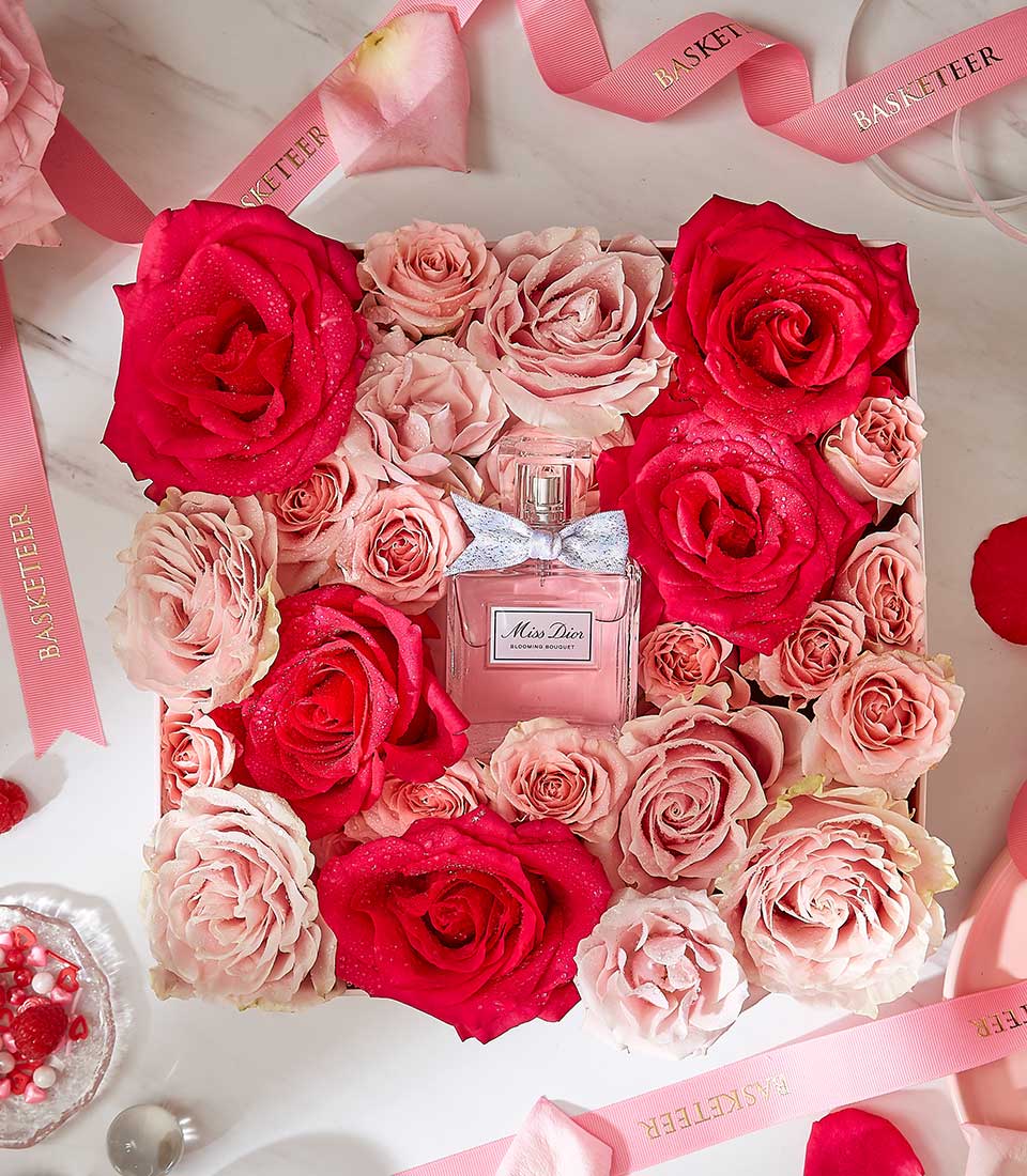 Luxury gift box with fresh pink and red roses, Miss Dior Blooming Bouquet perfume, and gold-branded ribbon