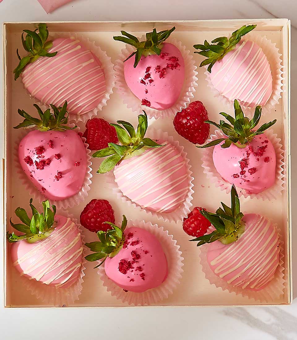 Pink chocolate-covered strawberries with white drizzle and raspberries in wooden gift box