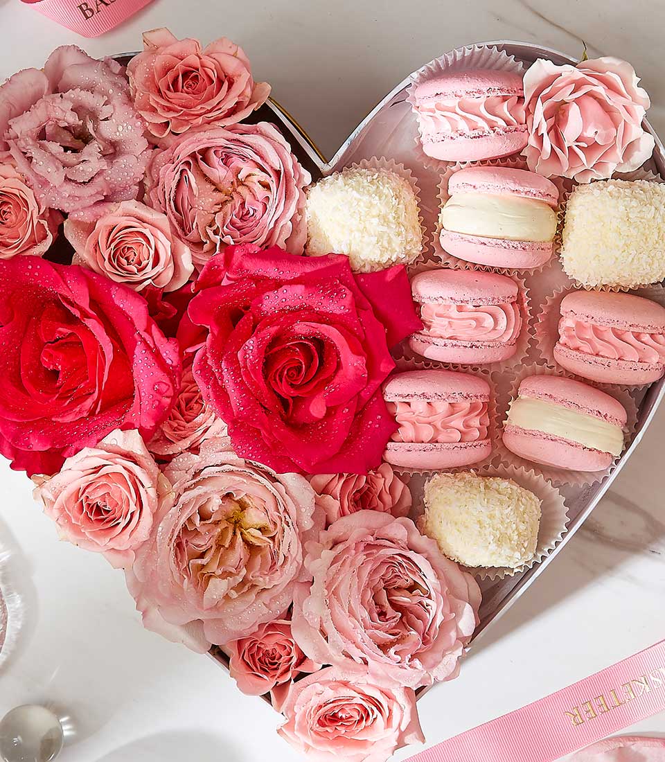 Heart-shaped gift box with fresh red and pink roses, pink macarons, and white truffles