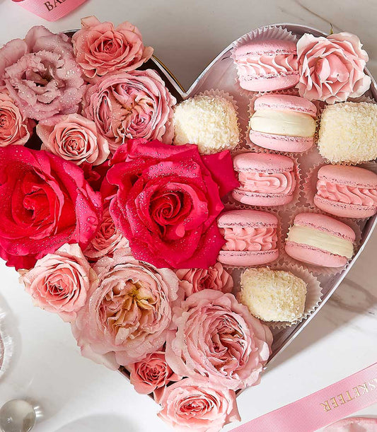 Heart-shaped gift box with fresh red and pink roses, pink macarons, and white truffles