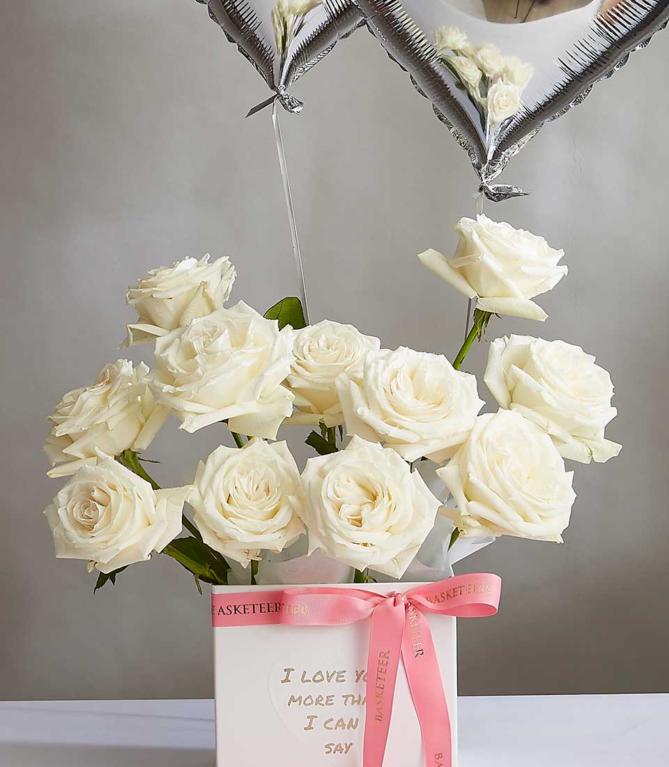 White rose bouquet in luxury gift box with heart balloons and pink ribbon for Valentine's Day