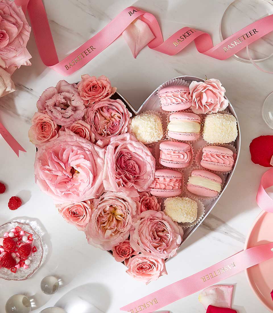 Heart-shaped gift box with fresh pink roses, pink macarons, and white confections for birthdays