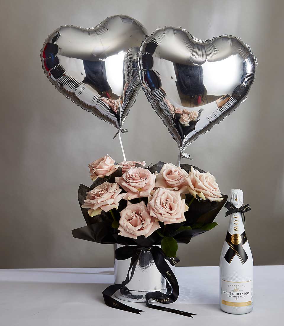 Light pink roses with champagne, silver heart balloons, and black ribbon for anniversary celebrations