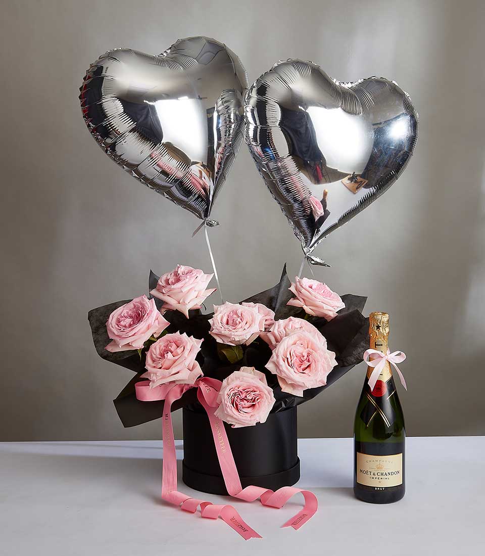 Blush roses in black hatbox with champagne, heart balloons, and pink ribbon for anniversary celebrations
