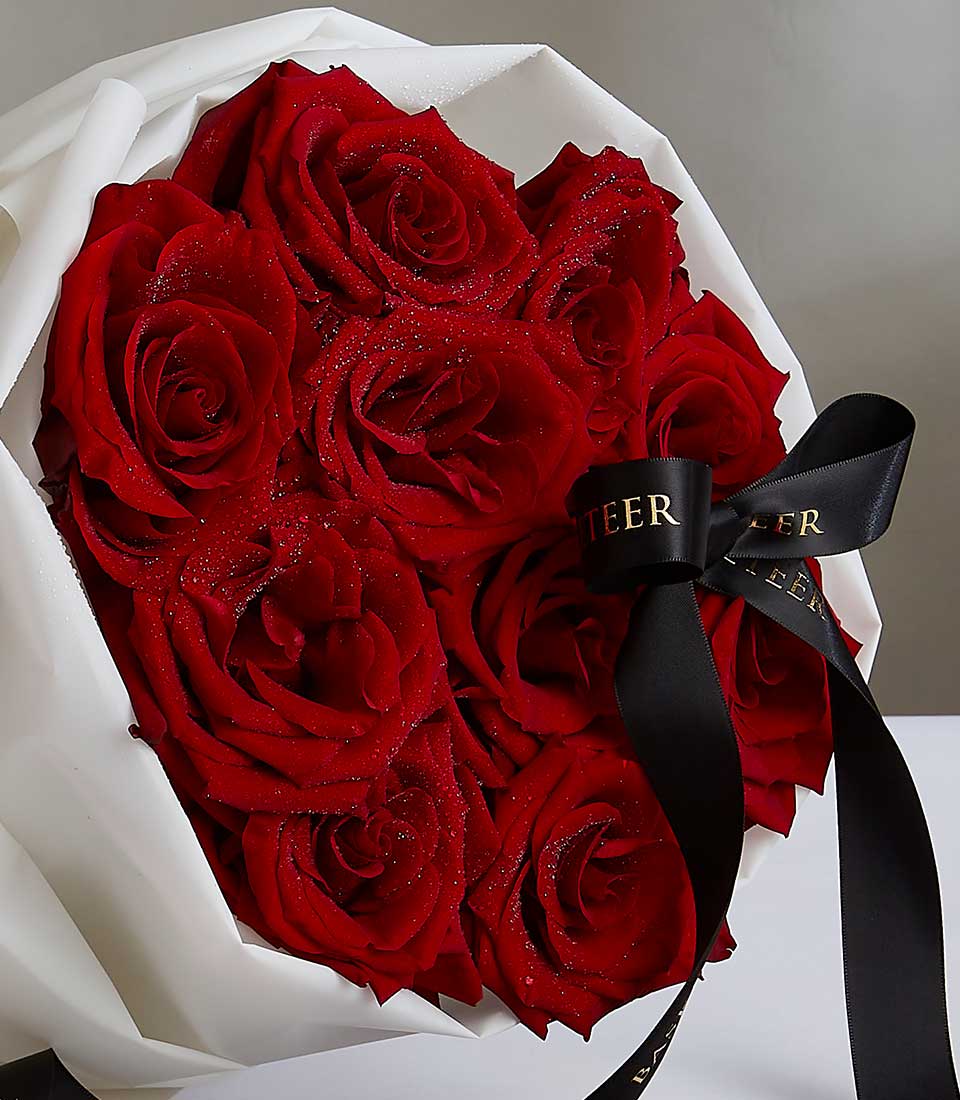 Vibrant red roses with water droplets, white paper wrap and black satin ribbon bow for Valentine's and anniversary