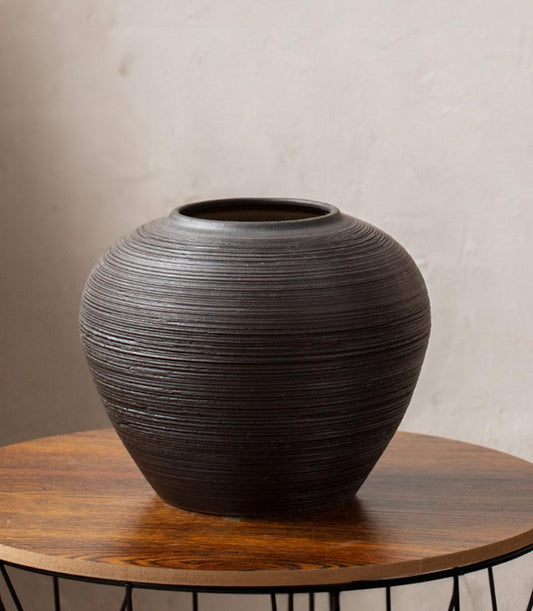 Dark striped ceramic vase with textured ridged surface on wooden side table
