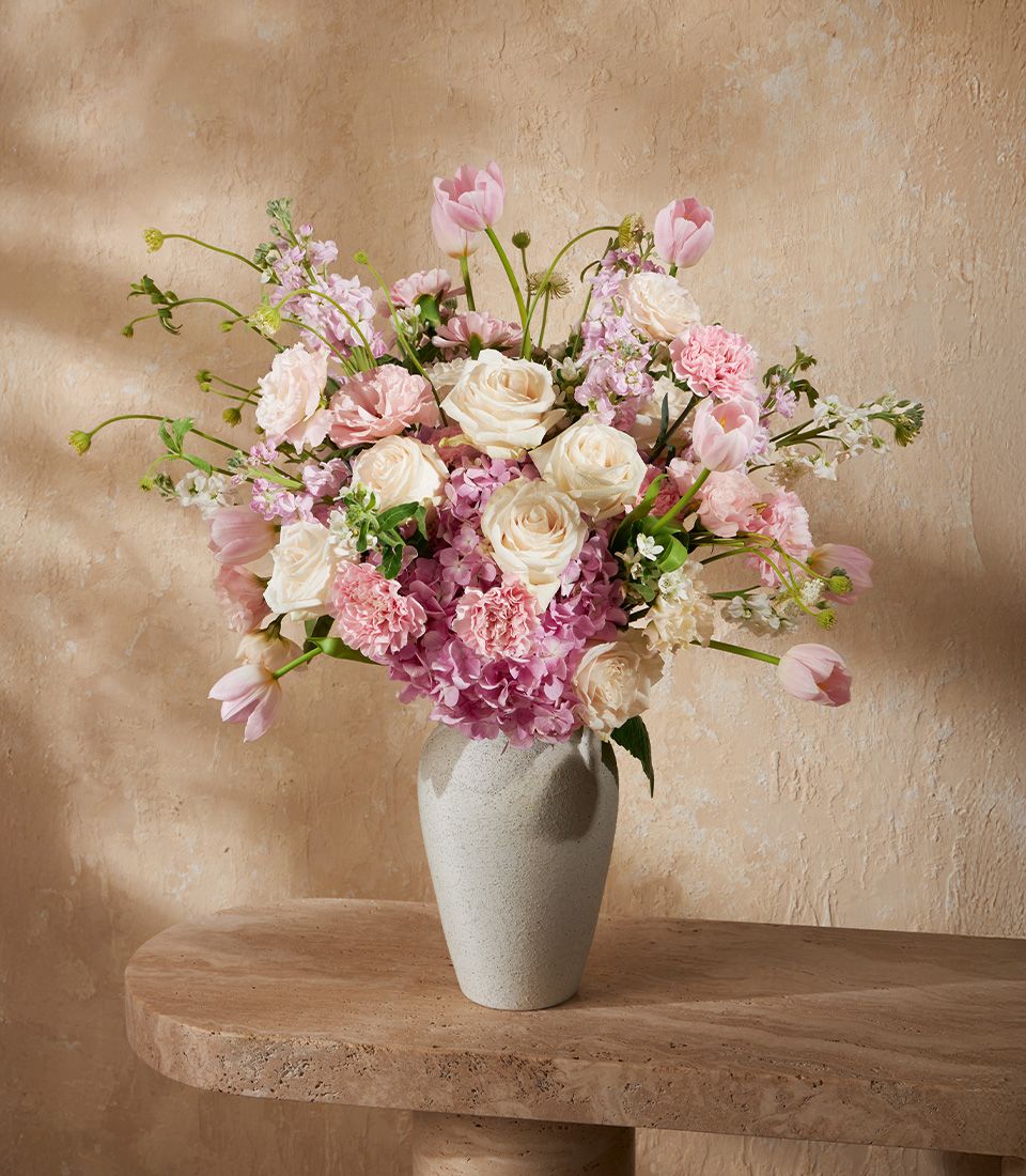 Pink and white floral arrangement with tulips, roses, and hydrangeas in grey ceramic vase