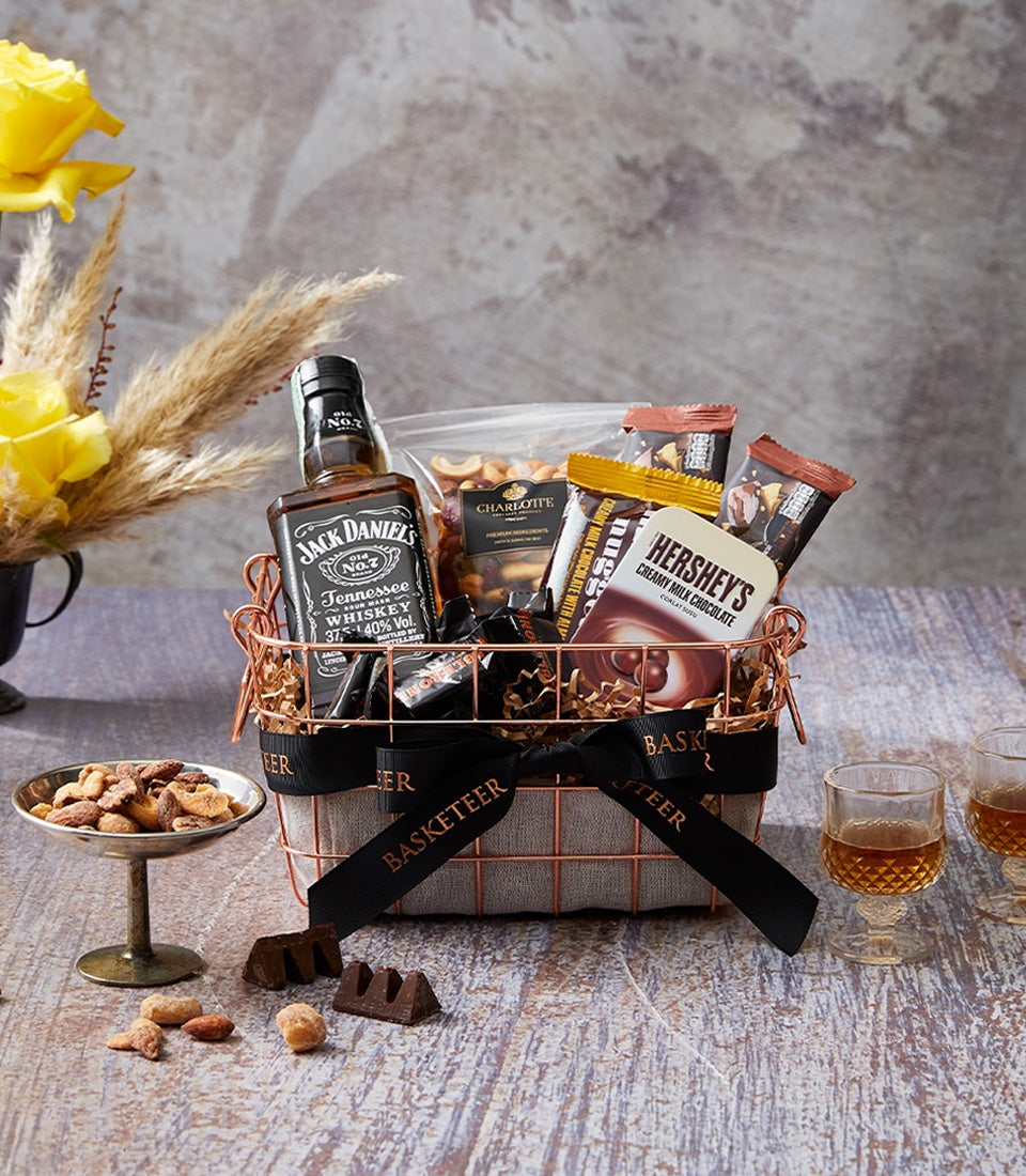 Premium whiskey gift basket with mixed nuts, chocolates, and cordial glasses on rustic wood