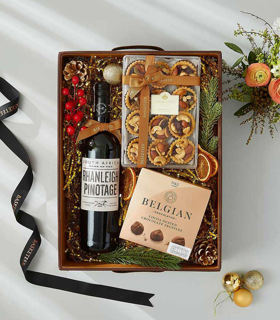 Premium festive wine gift hamper with Pinotage red wine, Belgian chocolates, and gourmet tarts on gold shredded paper