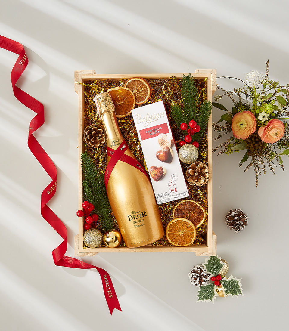 Festive gold champagne gift set with chocolate hearts, pine branches, and holiday decorations