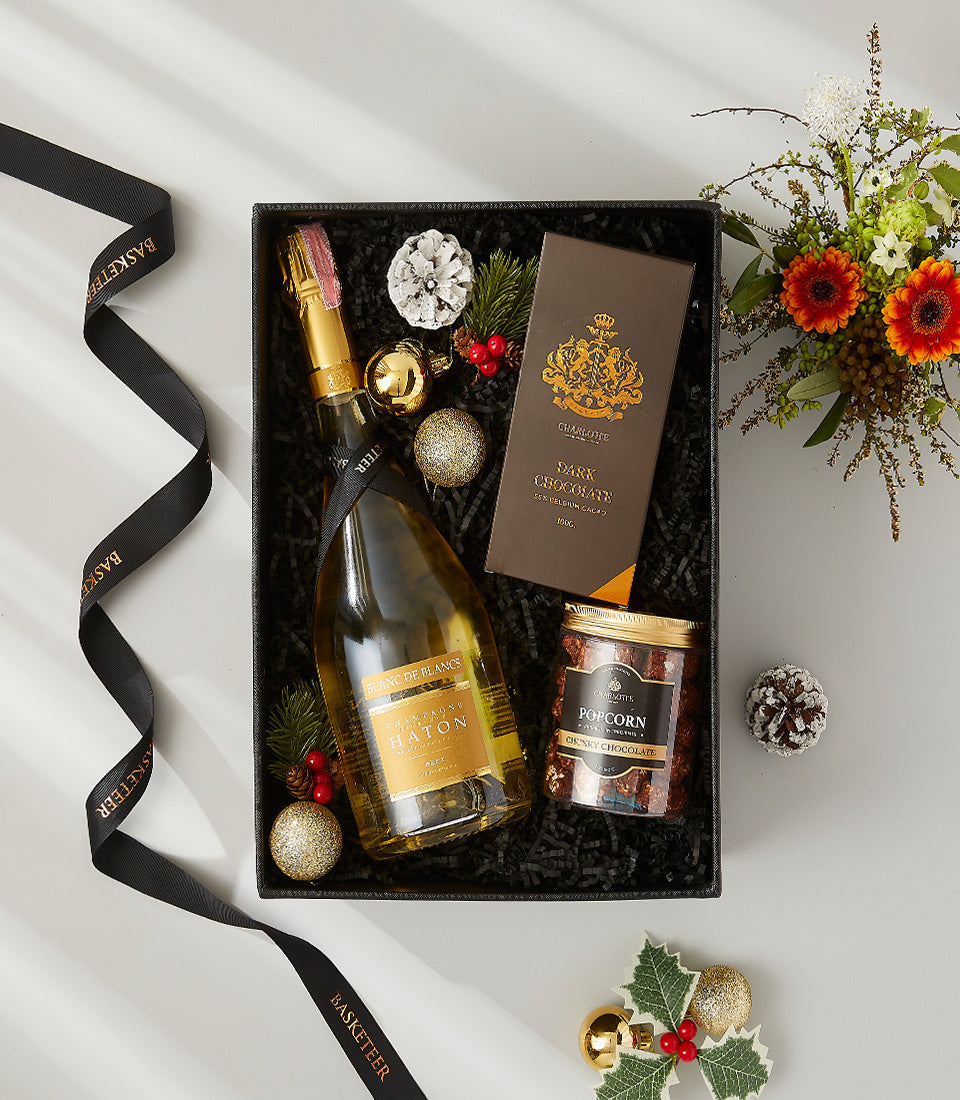 Luxury champagne and gourmet gift box with chocolate, popcorn, gold accents, and fresh gerbera daisies