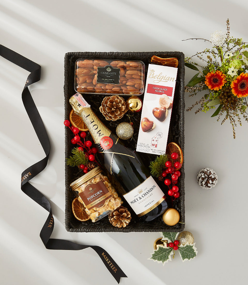 Premium champagne and gourmet gift basket with chocolate, almonds, and festive holiday decorations in dark woven basket