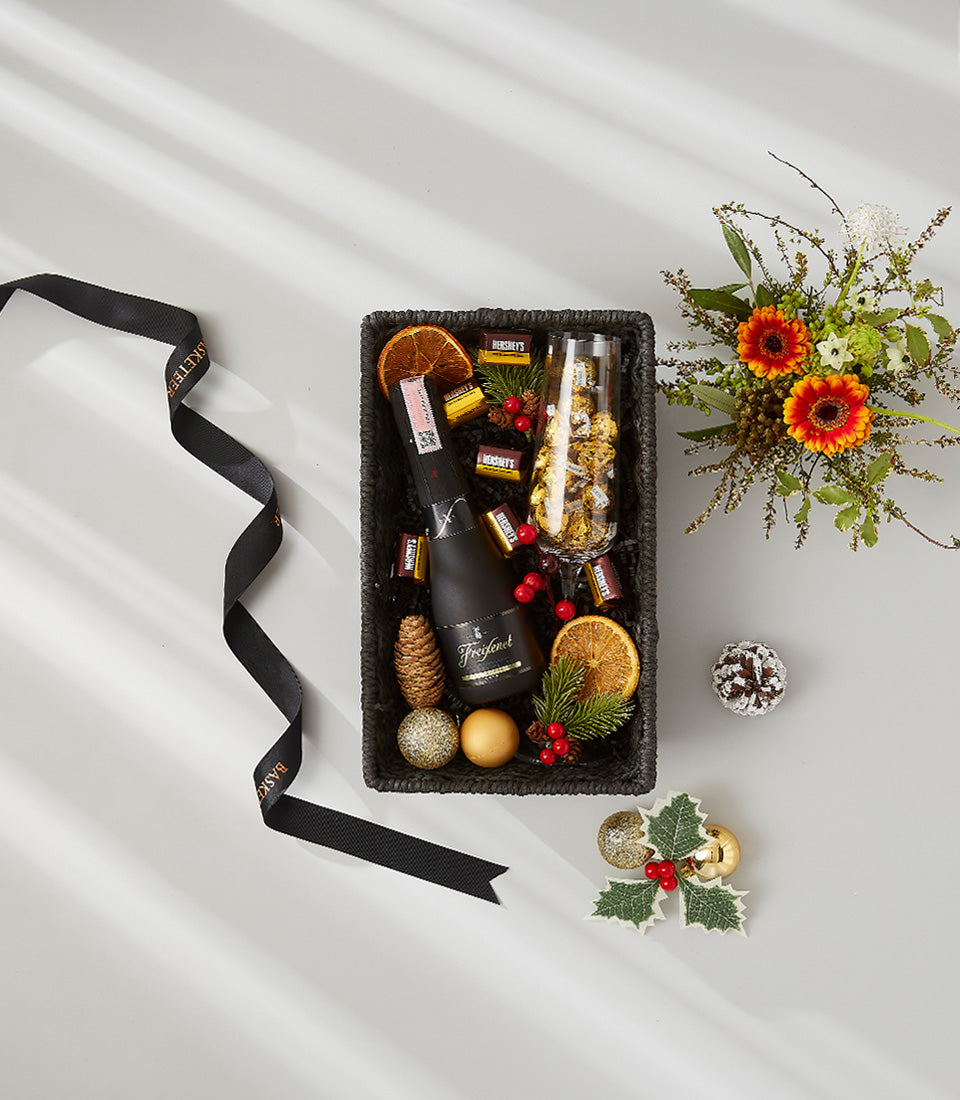 Luxury black woven gift basket with sparkling wine, Belgian chocolates, dried citrus, and holiday florals