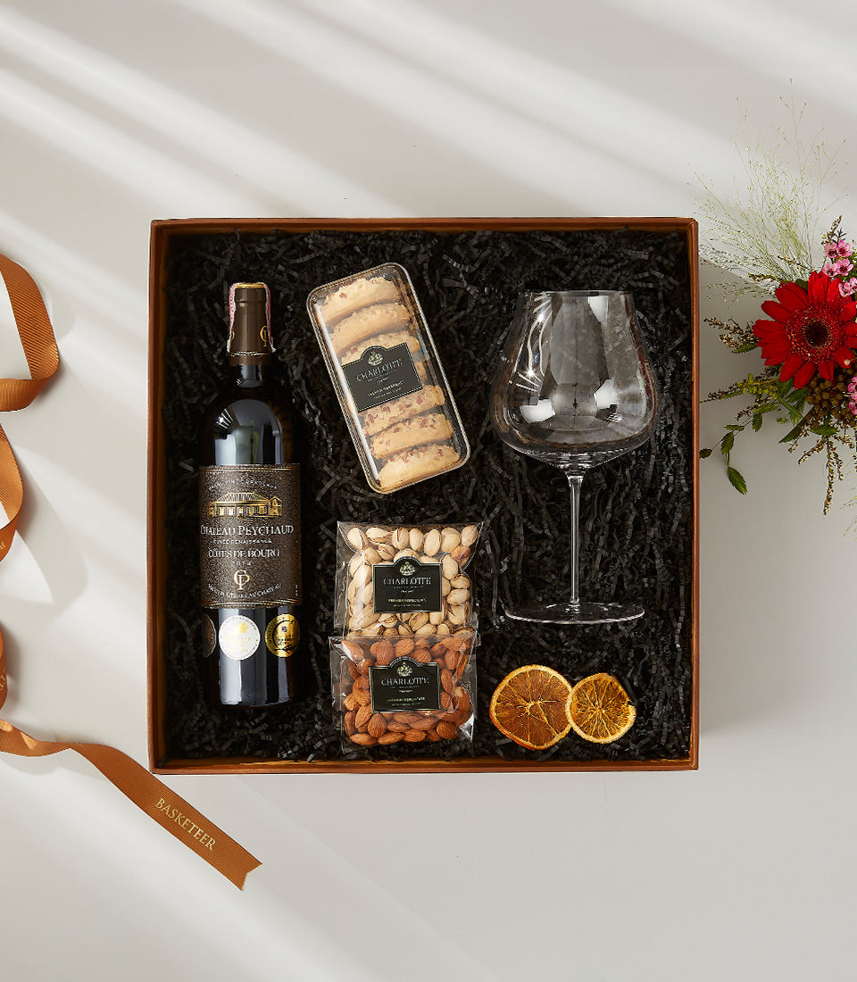 Premium wine gift set with red wine, gourmet biscotti, nuts, and stemmed glass in wooden box with red gerbera arrangement