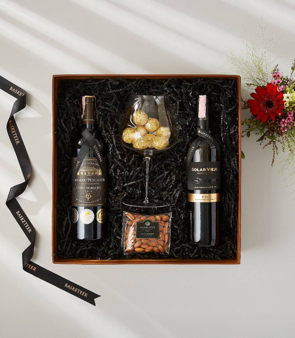 Luxury dark wood wine gift box with two premium red wines, chocolates in stemmed glass, roasted almonds, and fresh red