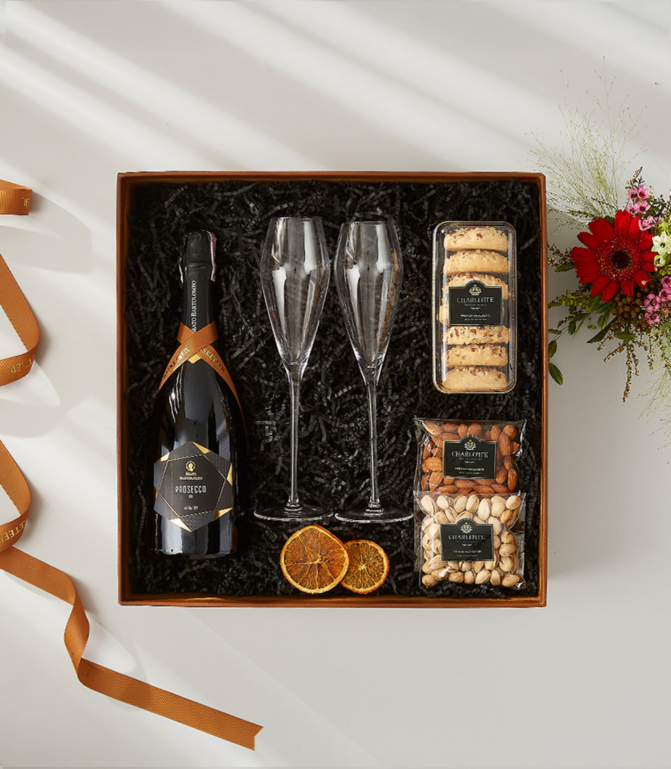 Prosecco celebration gift box with champagne flutes, gourmet nuts, cookies, and fresh florals