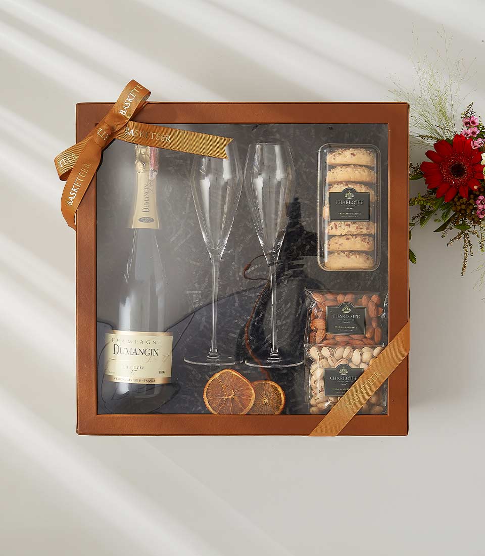 Champagne celebration gift box with flutes, gourmet treats, nuts, and dried orange on dark paper