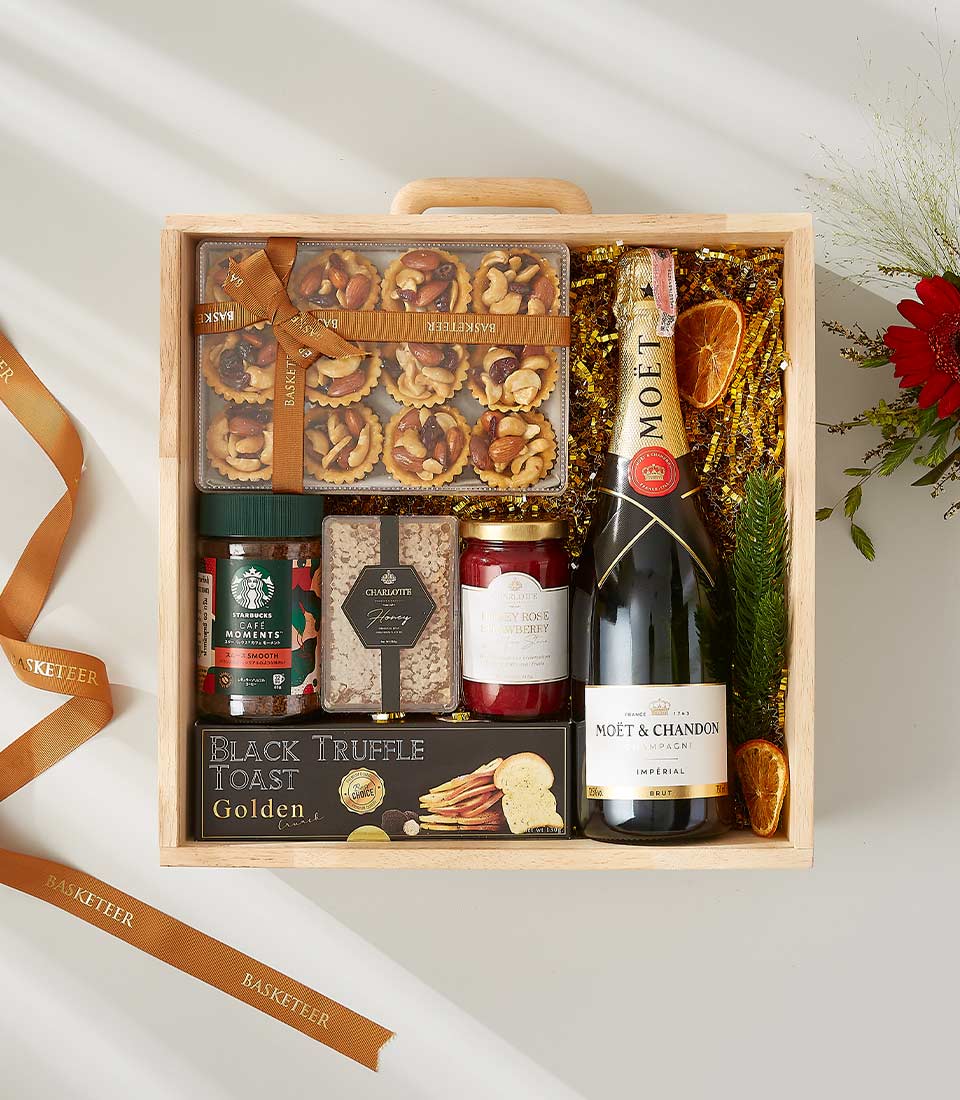 Luxury wooden gift box with Moët champagne, gourmet nuts, truffles, and artisan preserves on gold shredded paper