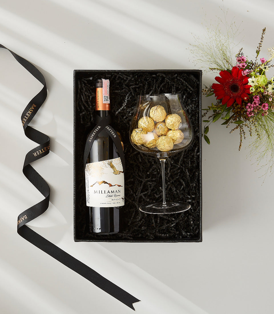 Premium red wine and gold-foiled chocolate gift set with red gerbera daisy bouquet in luxury black presentation box
