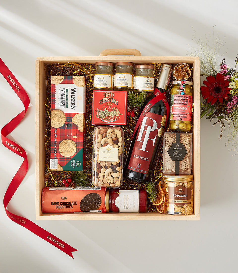 Premium wooden gift box with red wine, gourmet snacks, and festive trimmings on gold shredded paper