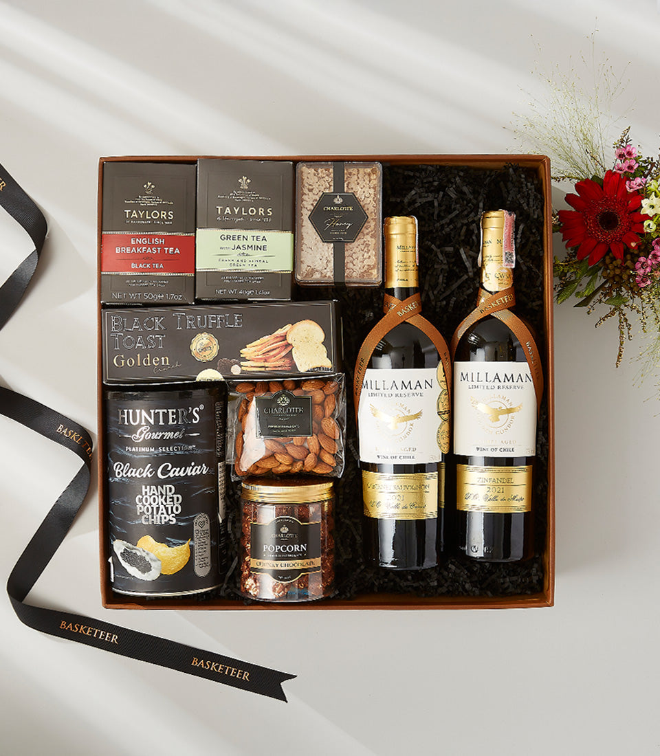 Luxury red wine gift box with gourmet pairings, tea, truffle toast, caviar chips, and artisan treats on black shredded paper