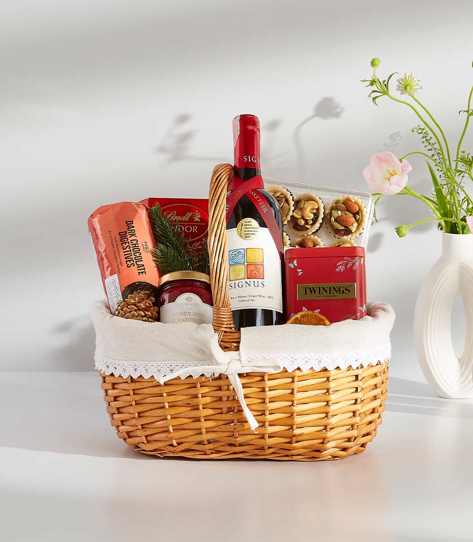 Wicker gift basket with red wine, gourmet tarts, chocolate, tea, and jam for thoughtful gifting