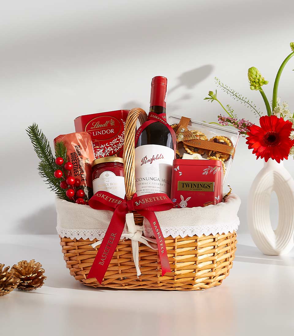 Luxury red wine gift basket with chocolates, jam, and gourmet treats, tied with red ribbon and displayed with fresh red