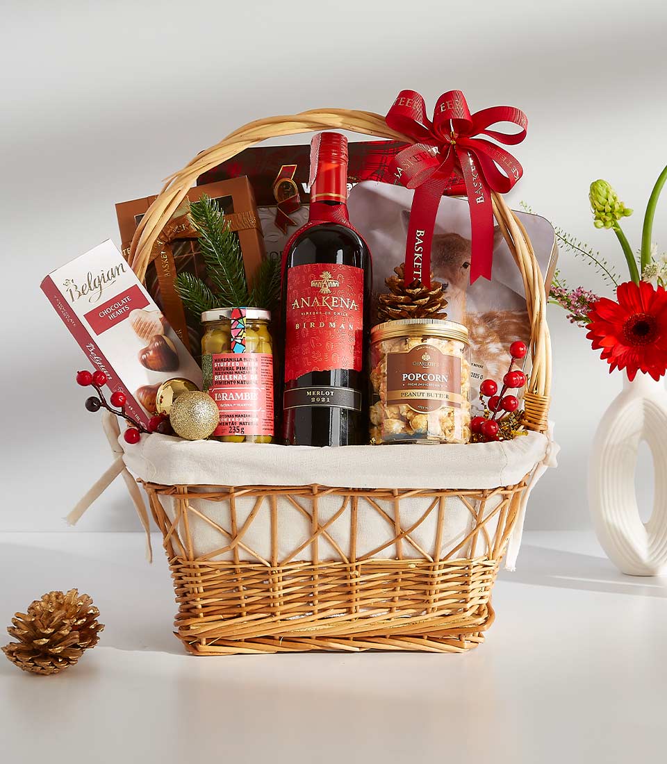 Premium wicker gift hamper with Merlot red wine, gourmet snacks, Belgian chocolate, and festive holiday decoration