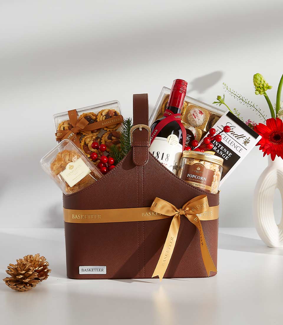 Brown leather gift basket with 1818 Classic red wine, chocolate, gourmet snacks, and festive berries