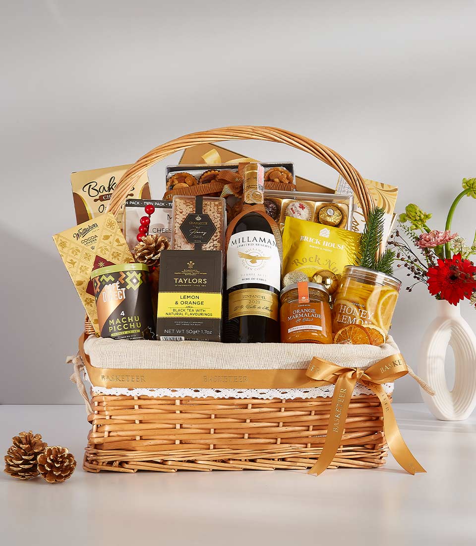 Festive wine gift basket with red wine, gourmet chocolates, tea, nuts, and spreads in wicker with gold ribbon